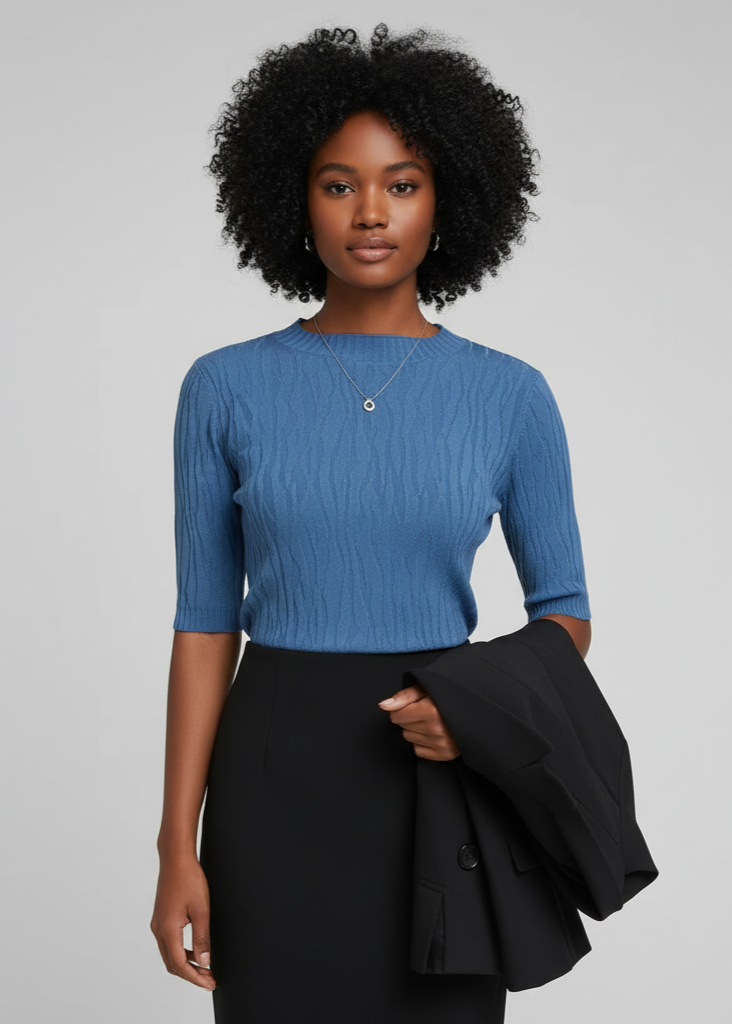 Woman wearing a blue top and black skirt holding a black jacket against a gray background