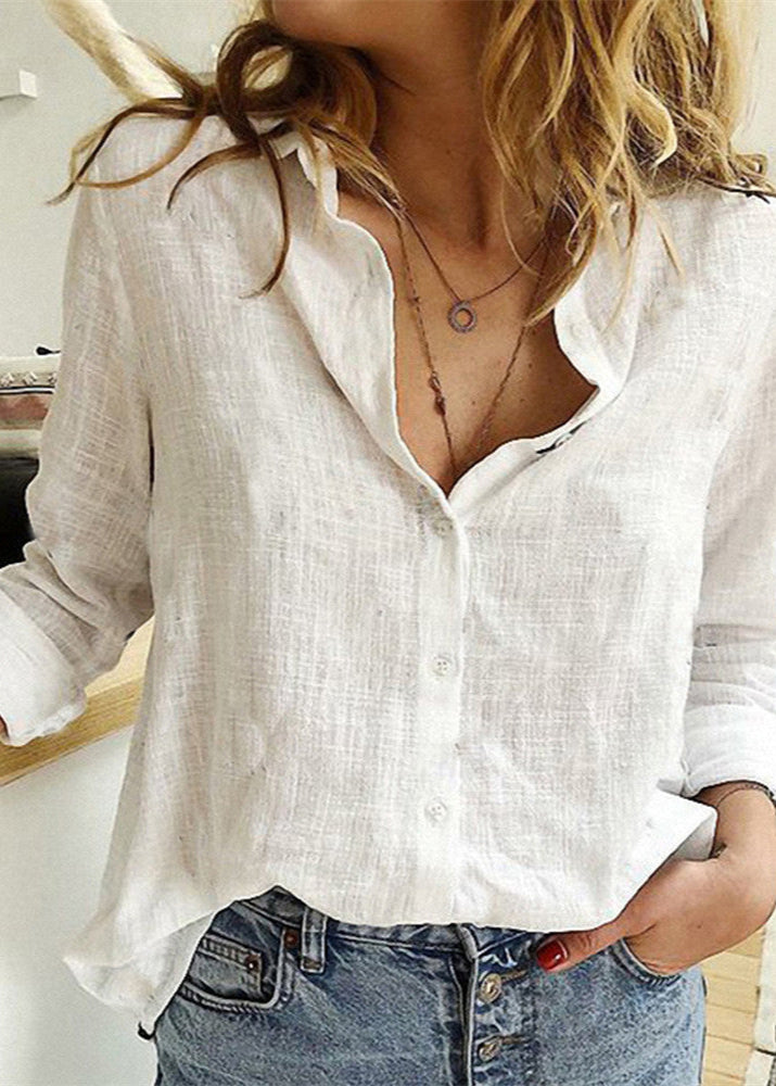 Person wearing a white linen shirt with rolled-up sleeves and denim jeans indoors.