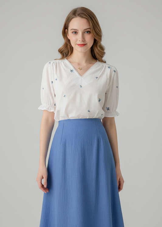 Woman wearing a white blouse with floral patterns and a blue skirt on a gray background