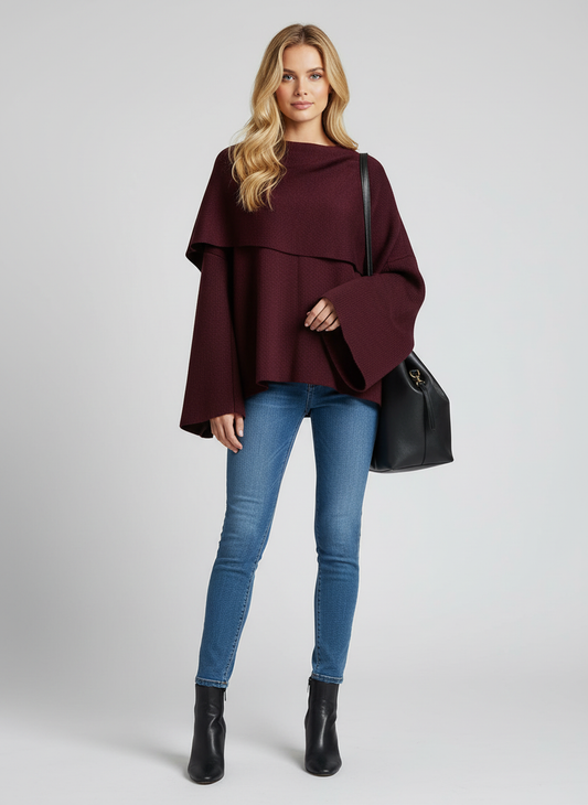 Woman wearing a burgundy poncho, blue jeans, and black boots on a light gray background