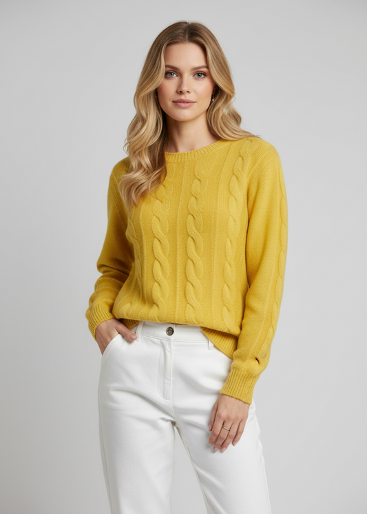 Woman wearing a mustard yellow cable knit sweater and white pants on a plain background