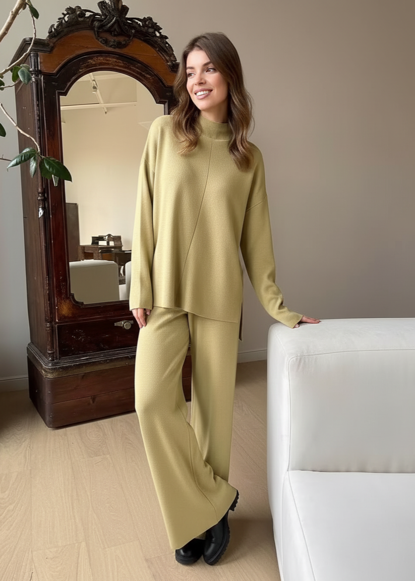 Woman in a light green outfit standing in a room with a white sofa and wooden mirror.