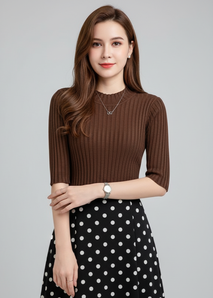 Woman wearing a brown ribbed sweater and black polka dot skirt on a gray background