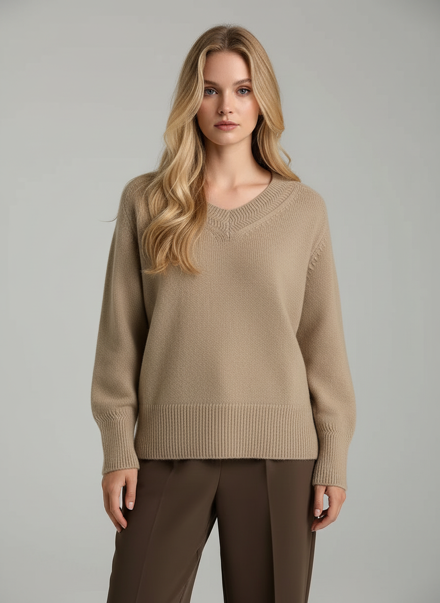 Woman wearing a beige sweater and brown pants against a gray background