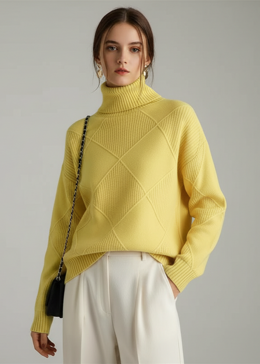 Woman wearing a yellow turtleneck sweater and white pants against a gray background