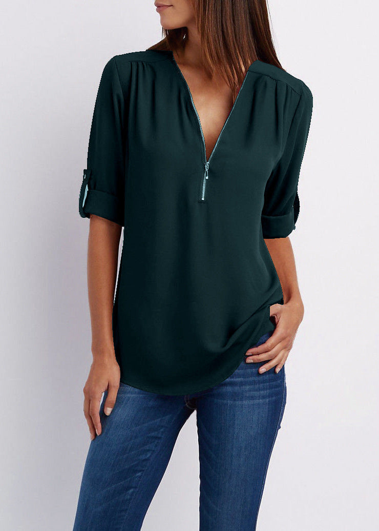 Person wearing a dark green blouse with a deep neckline and blue jeans on a light gray background