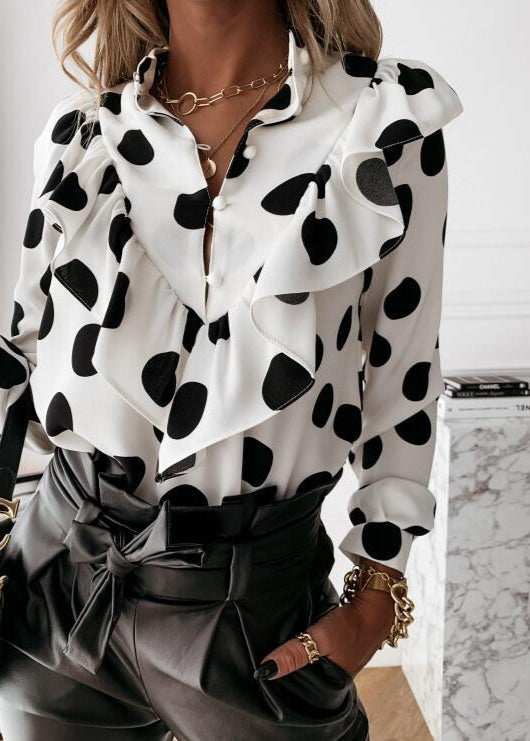 Person wearing a white blouse with black polka dots and gray pants in an indoor setting.