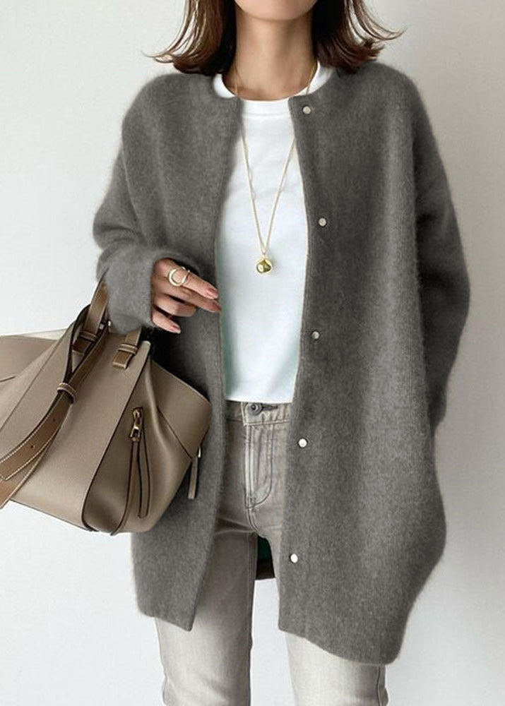 Person wearing a gray cardigan holding a beige handbag on a plain background