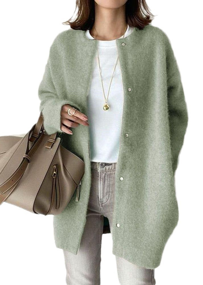 Person wearing a green cardigan holding a beige handbag on a white background