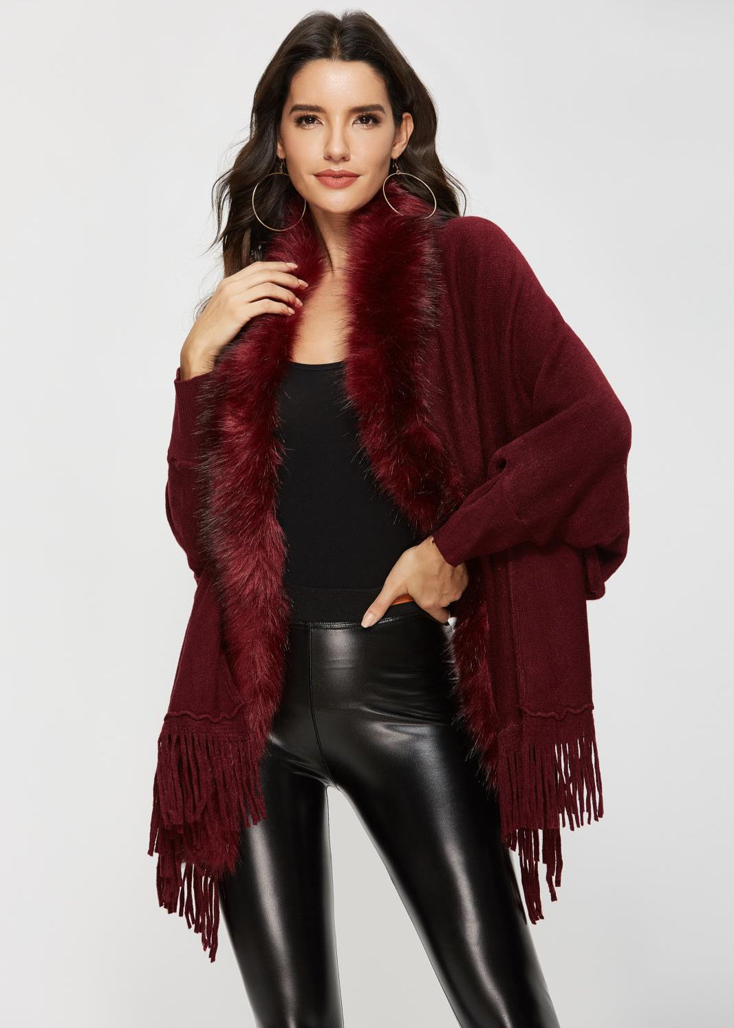 Woman wearing a burgundy fringed cardigan over a black top and leather pants on a white background