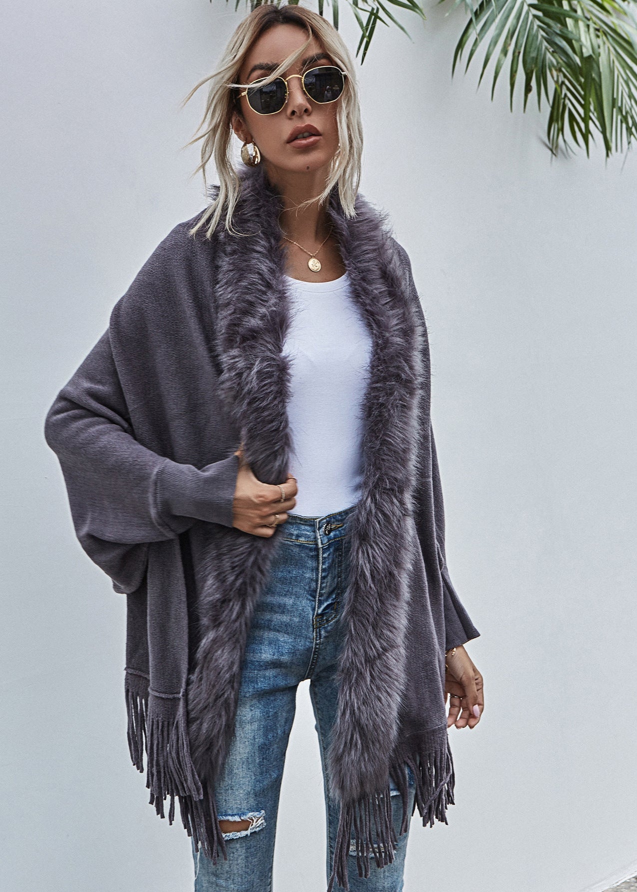 Woman wearing a gray fringe cardigan with a fur collar against a light background