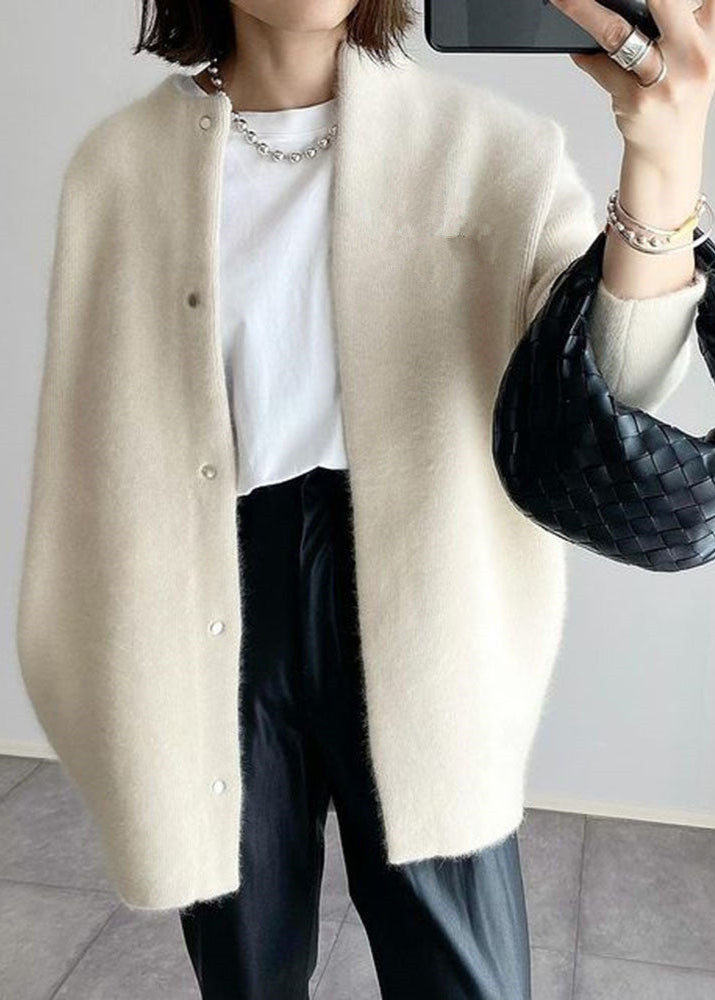 Person wearing a beige cardigan, white shirt, black pants, and holding a black handbag.