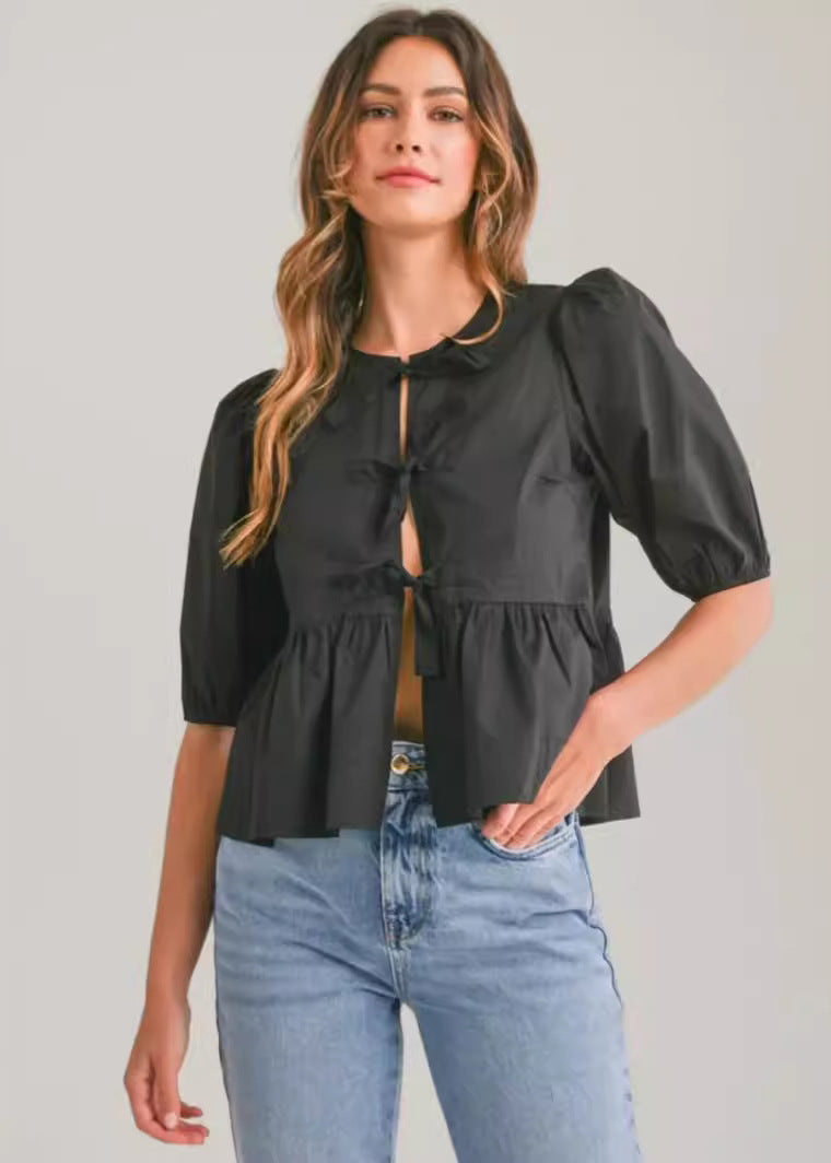 Woman wearing a black blouse with puff sleeves and blue jeans on a plain background