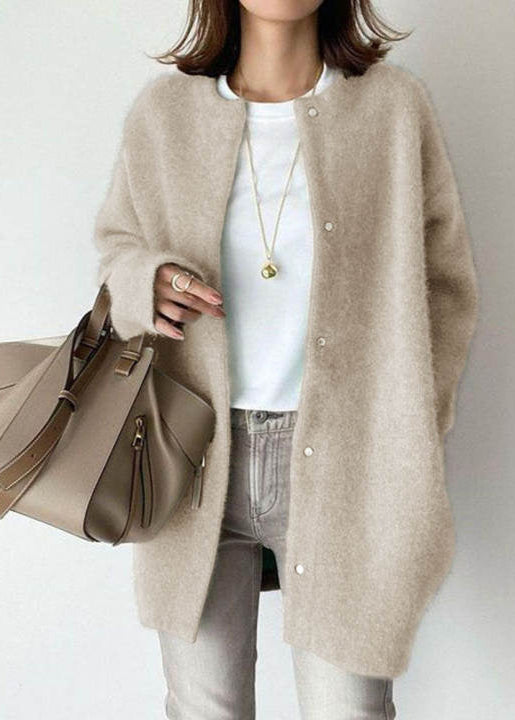 Person wearing a beige cardigan holding a matching handbag against a plain background
