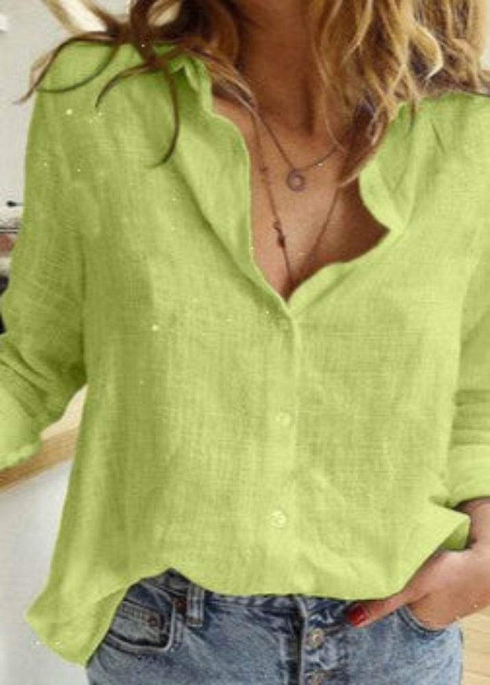 Person wearing a light green blouse with rolled-up sleeves and denim shorts indoors.