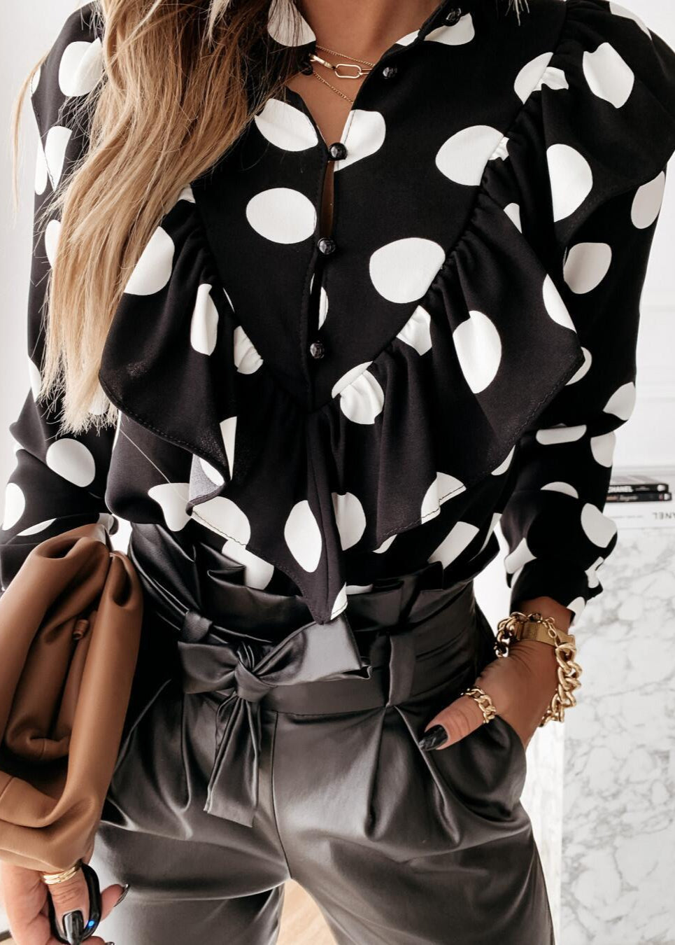 Person wearing a black and white polka dot blouse with gray pants, holding a brown bag.