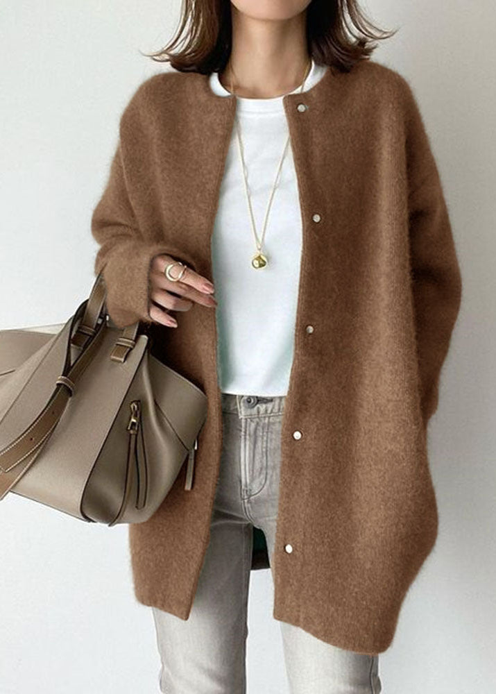 Person wearing a brown cardigan holding a beige handbag on a plain background