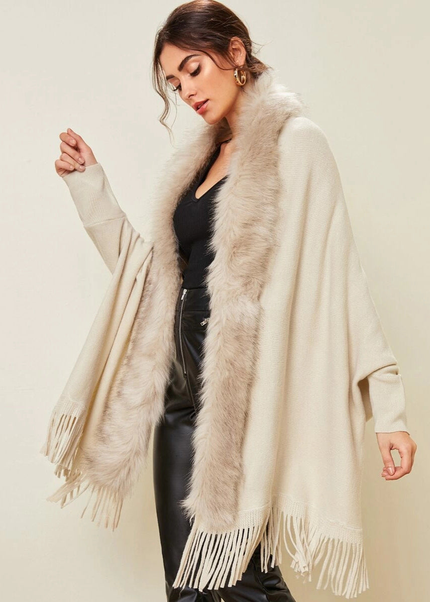 Woman wearing a beige fringed poncho with fur trim against a plain background