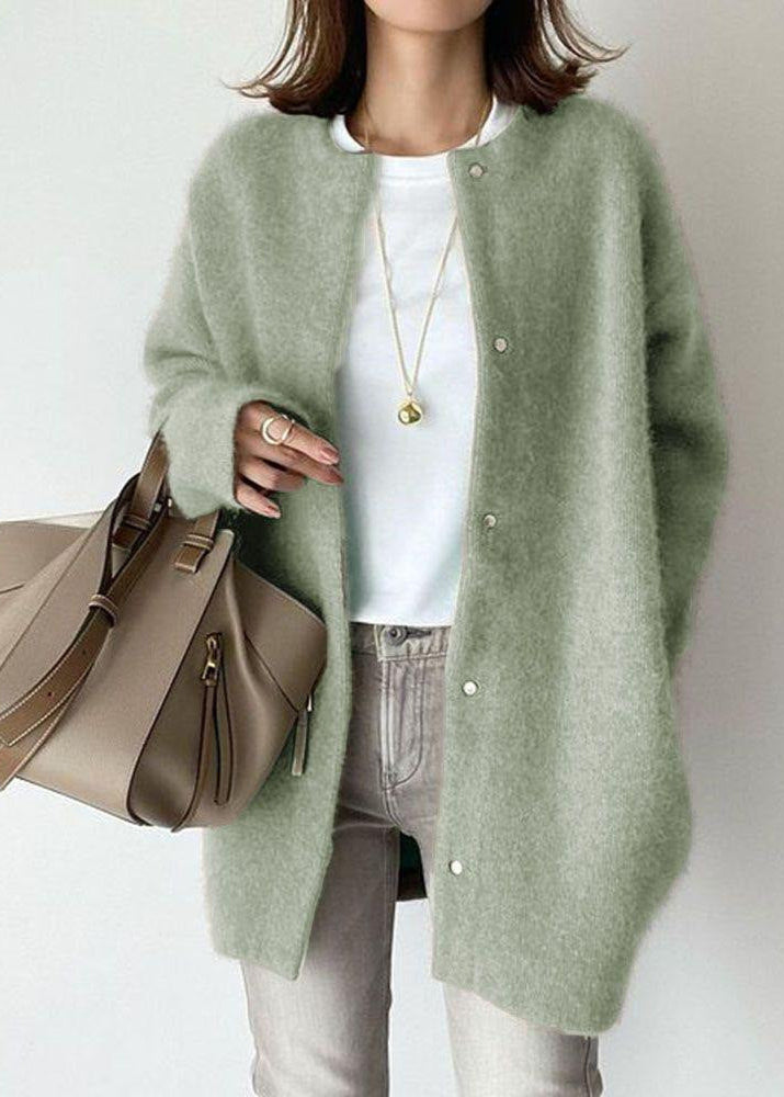Person wearing a green cardigan holding a beige handbag on a plain background