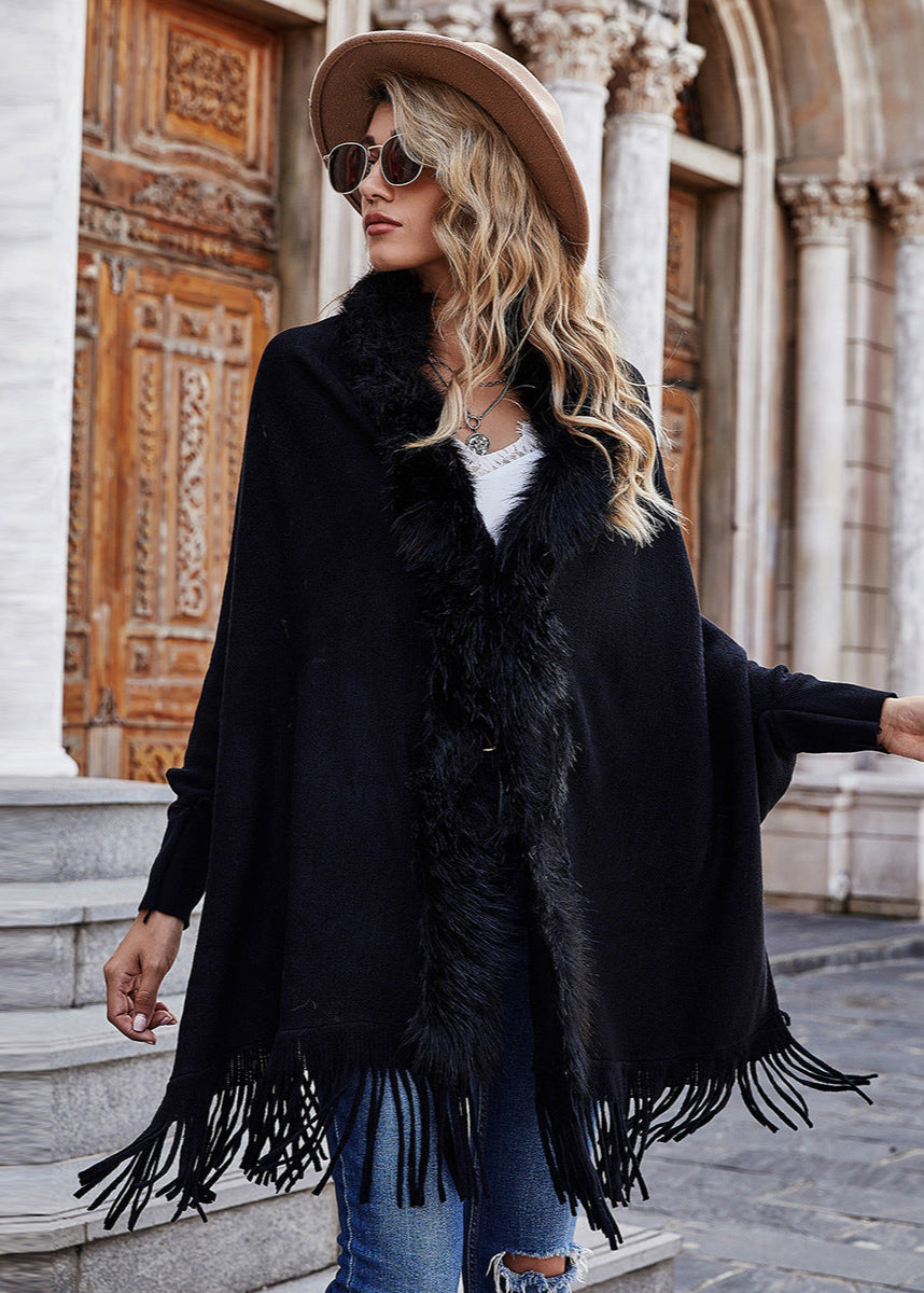 Woman wearing a black fringed poncho, blue jeans, and a beige hat in an urban setting.