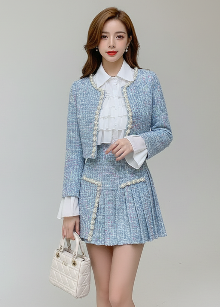 Woman wearing a light blue tweed suit with a white shirt and holding a white handbag on a gray background